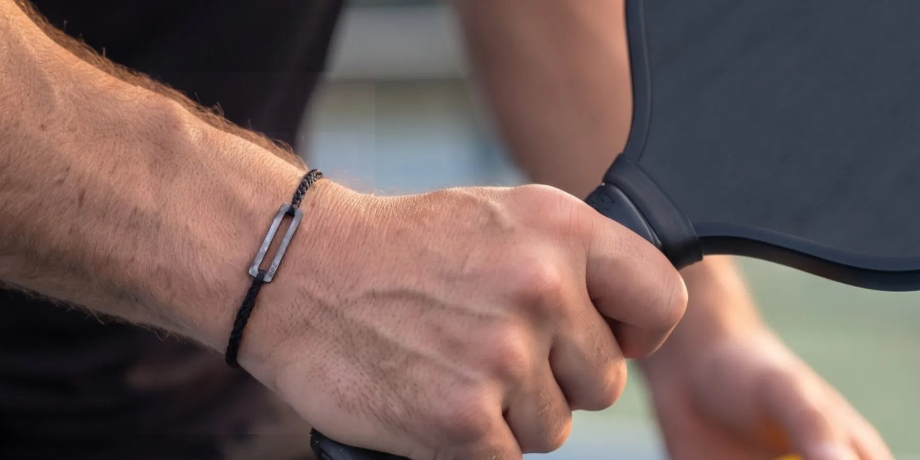 a man holding a black paddle and wearing a black pickleball bracelet