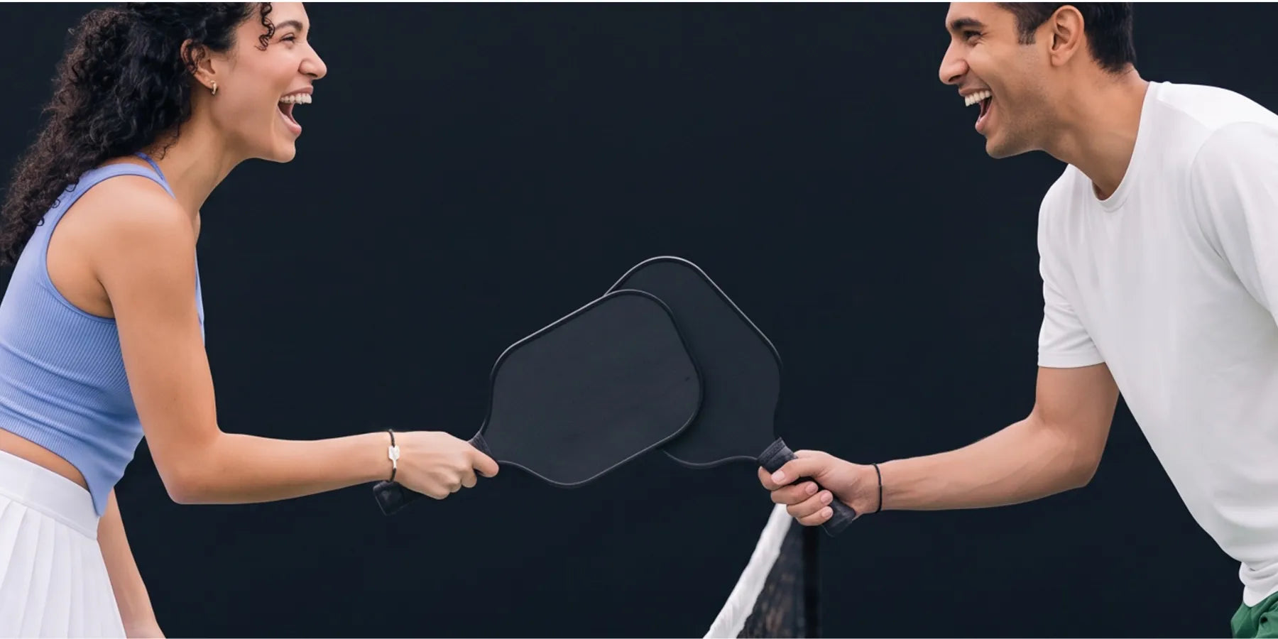pickleball partners tapping paddles on a pickleball court, laughing and wearing the matching bracelets