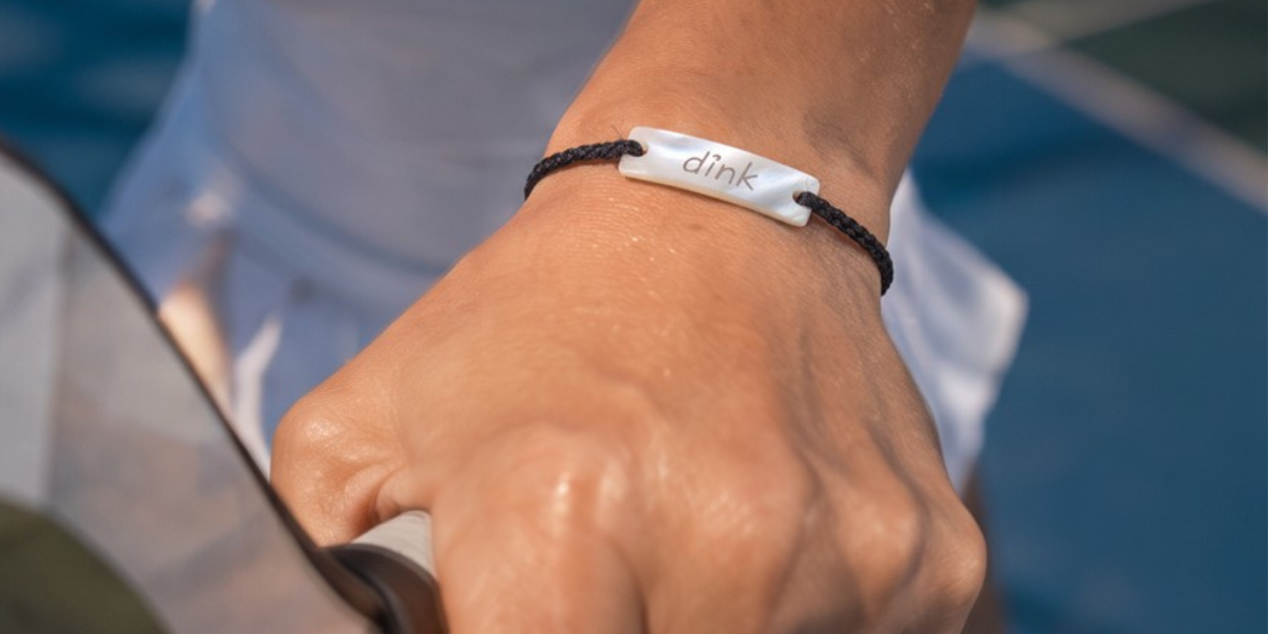 a black cord bracelet with a "dink" stone charm on a wrist