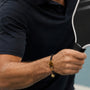 Person wearing a black shirt and pickleball bracelet holding a black and white paddle.