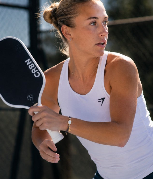 Woman holding a pickleball paddle on a court and wearing a string pickleball bracelet with a white paddle charm
