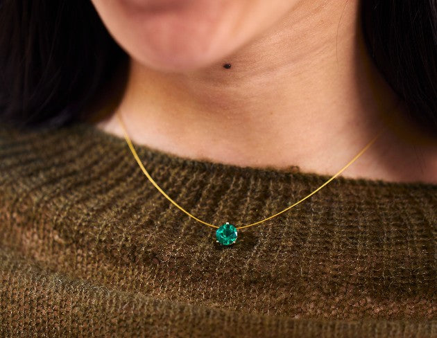 Person wearing a gold nylon necklace with an emerald on a brown sweater.