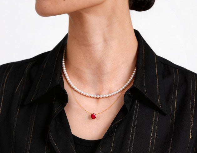 Person wearing a pearl necklace and a ruby necklace on a plain background