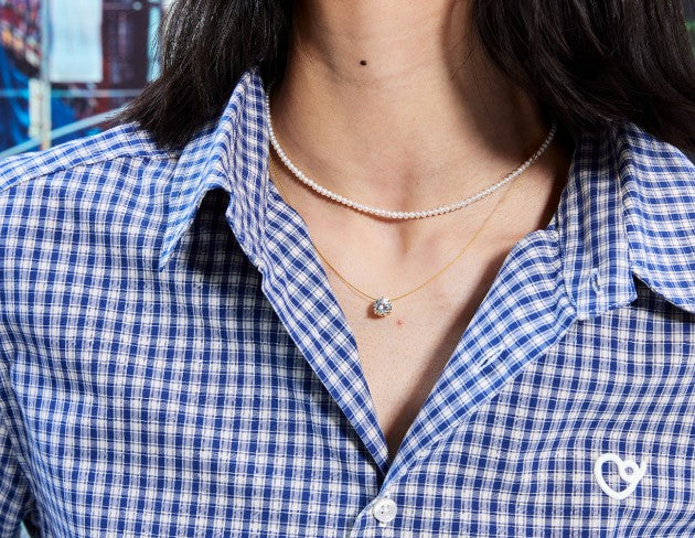 Person wearing a blue and white checkered shirt with layered necklaces.
