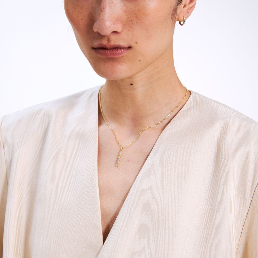 Close-up of a person wearing a gold bar necklace with a plain background