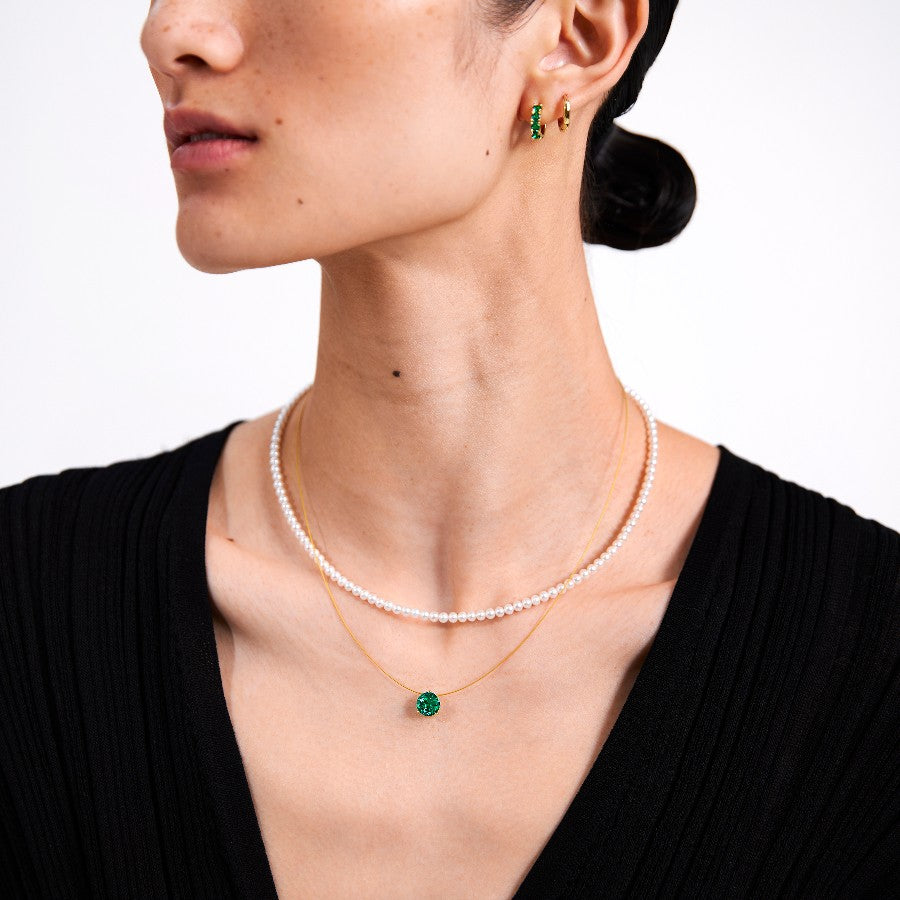 Woman wearing a pearl necklace, emerald necklace and green emerald earrings on a white background