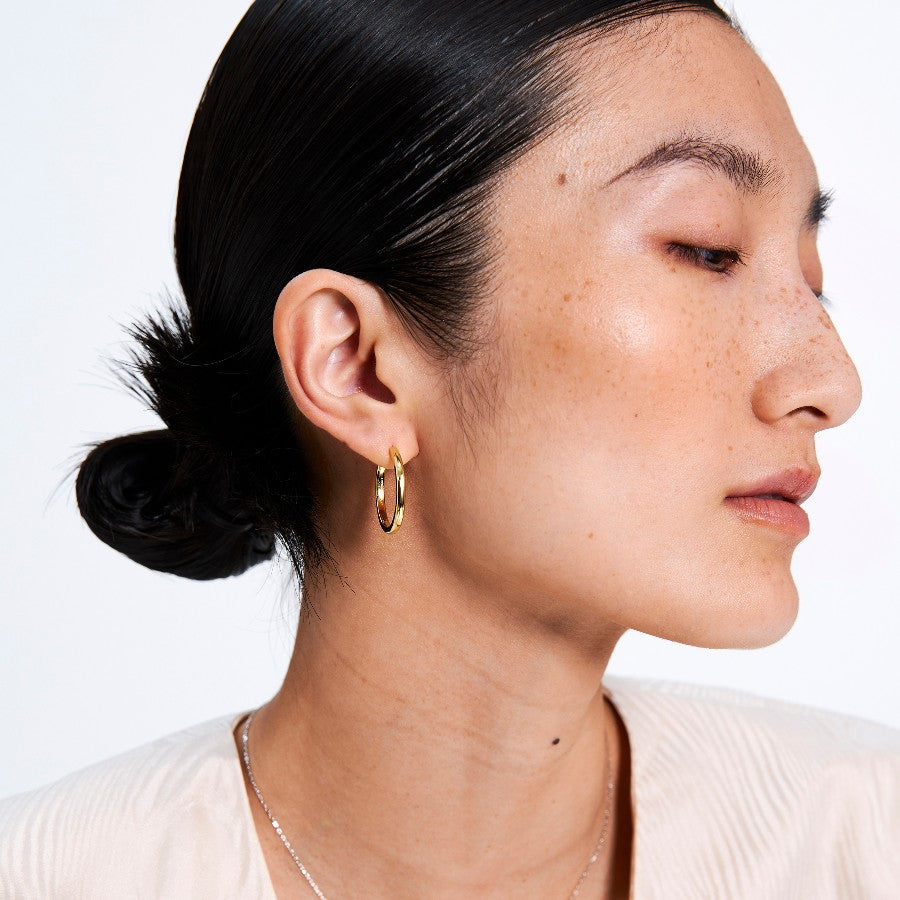 Close-up of a person wearing a gold hoop earring on a white background