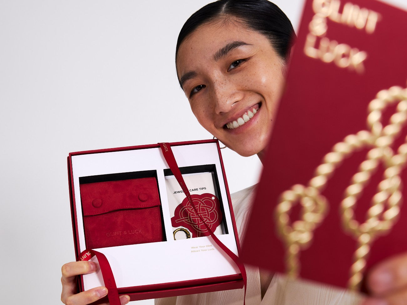 Person holding a red jewelry box with a card inside, smiling.