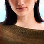 Close-up of a person wearing a gold nylon necklace with a green gemstone pendant.