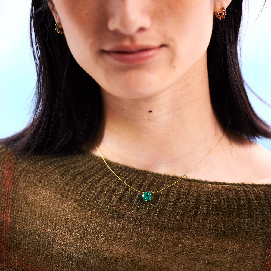 Close-up of a person wearing a gold nylon necklace with a green gemstone pendant.