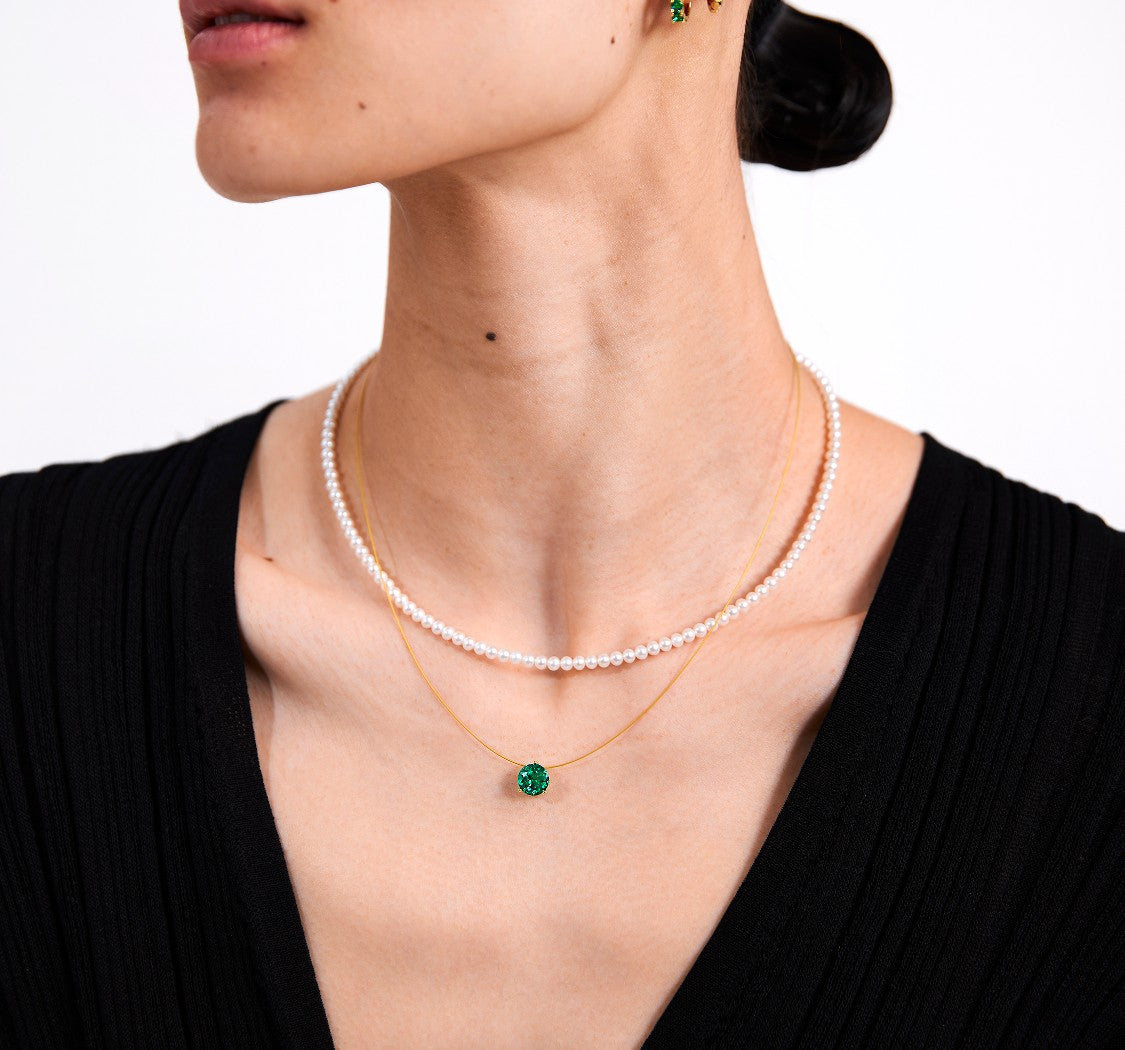 Pearl necklace and emerald necklace on a model against a white background