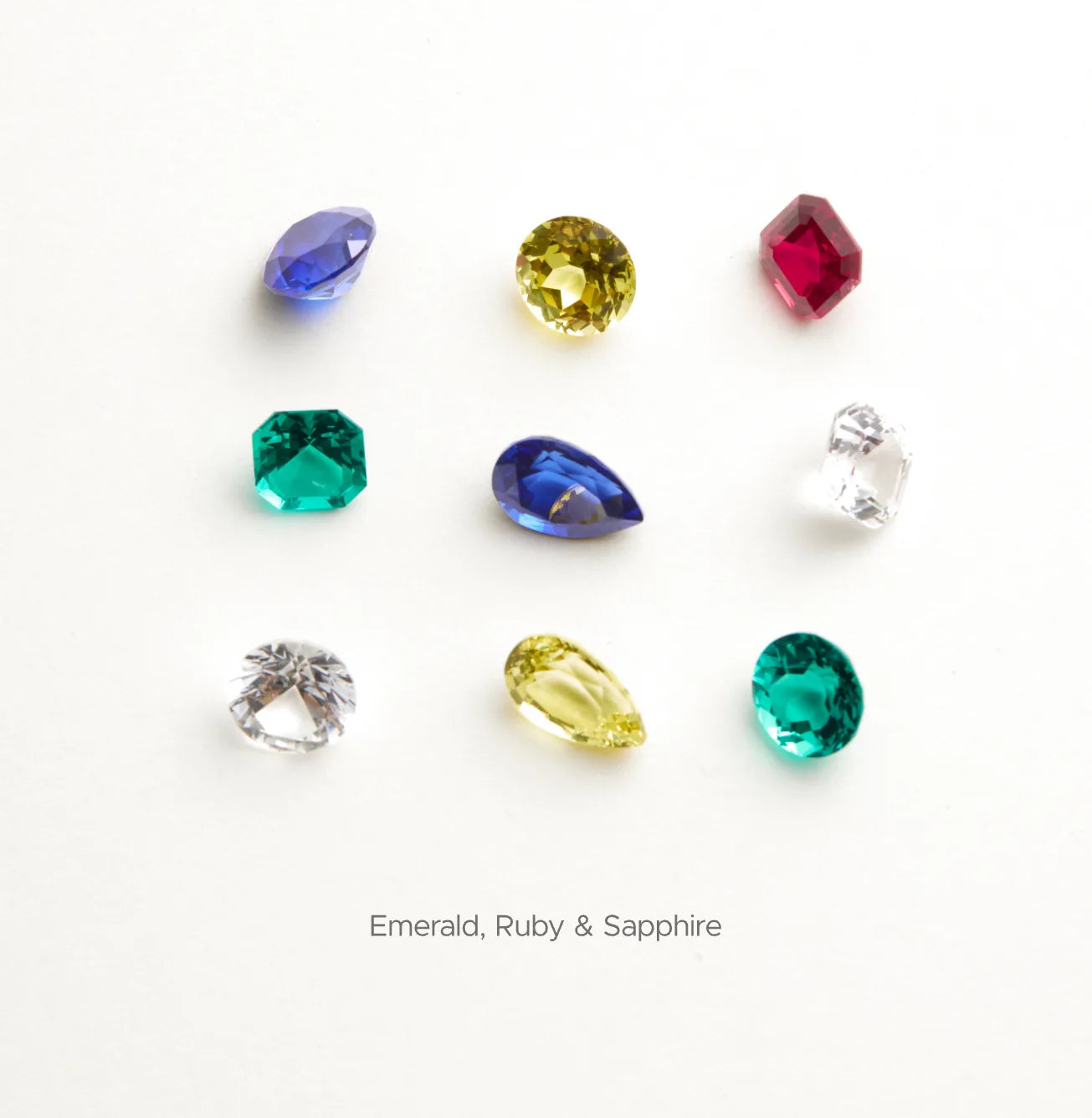 Collection of gemstones including emerald, ruby, and sapphire on a white background.