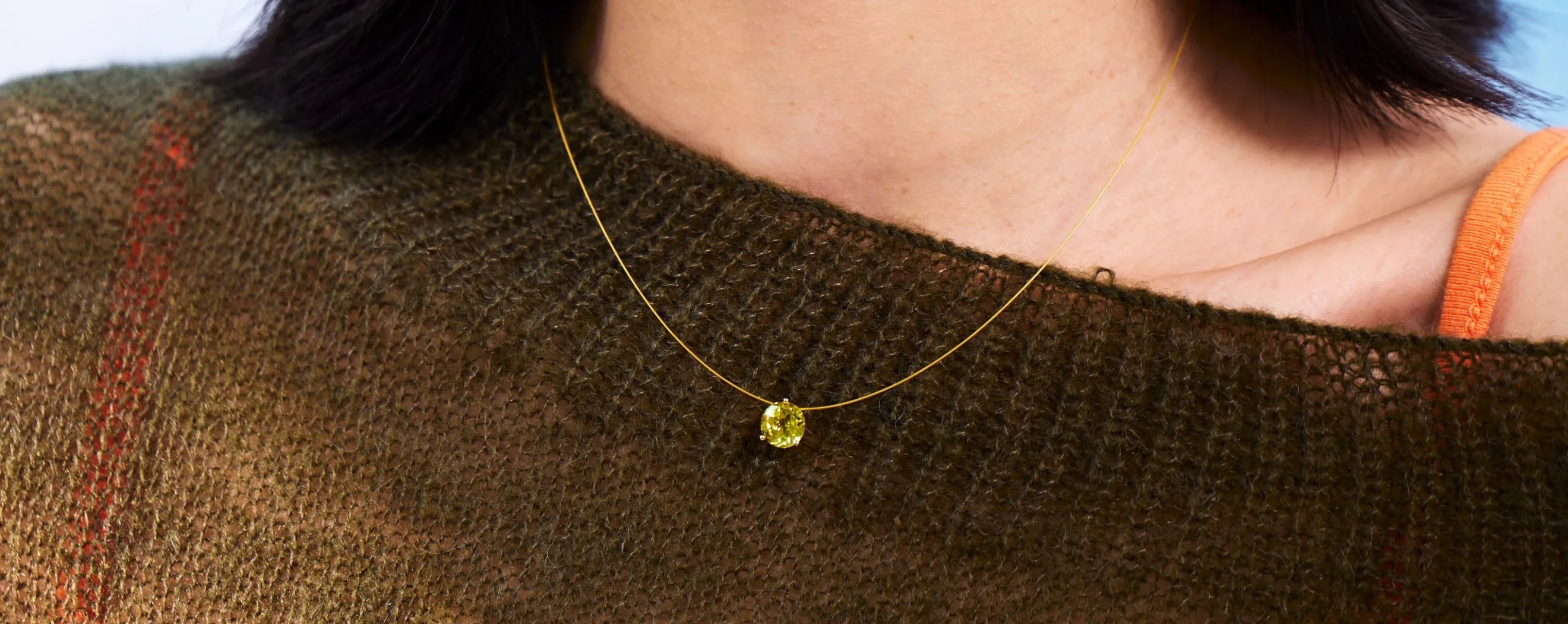Close-up of a person wearing a gold necklace with a yellow gemstone.