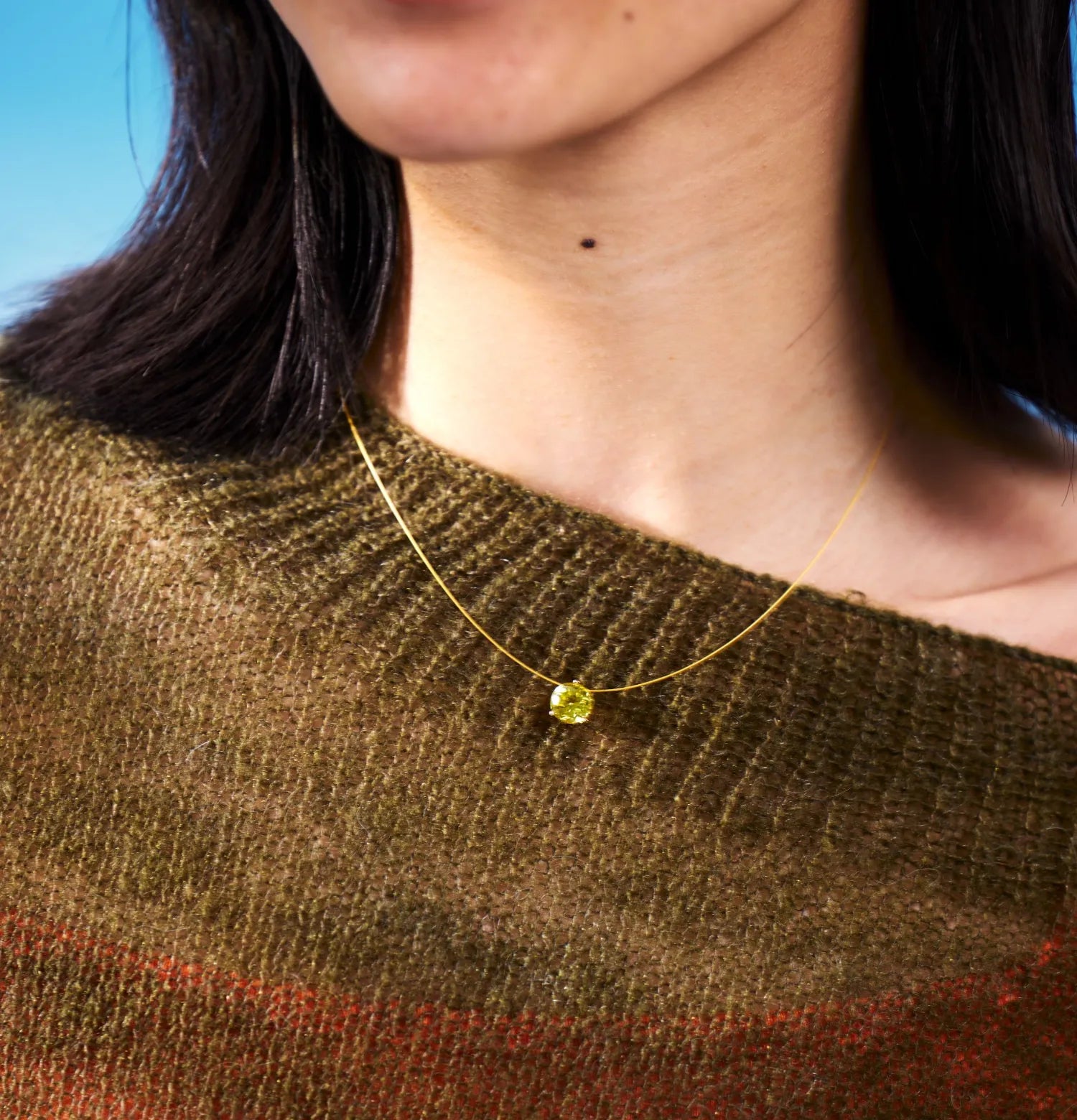 Close-up of a person wearing a gold necklace with a yellow gemstone 