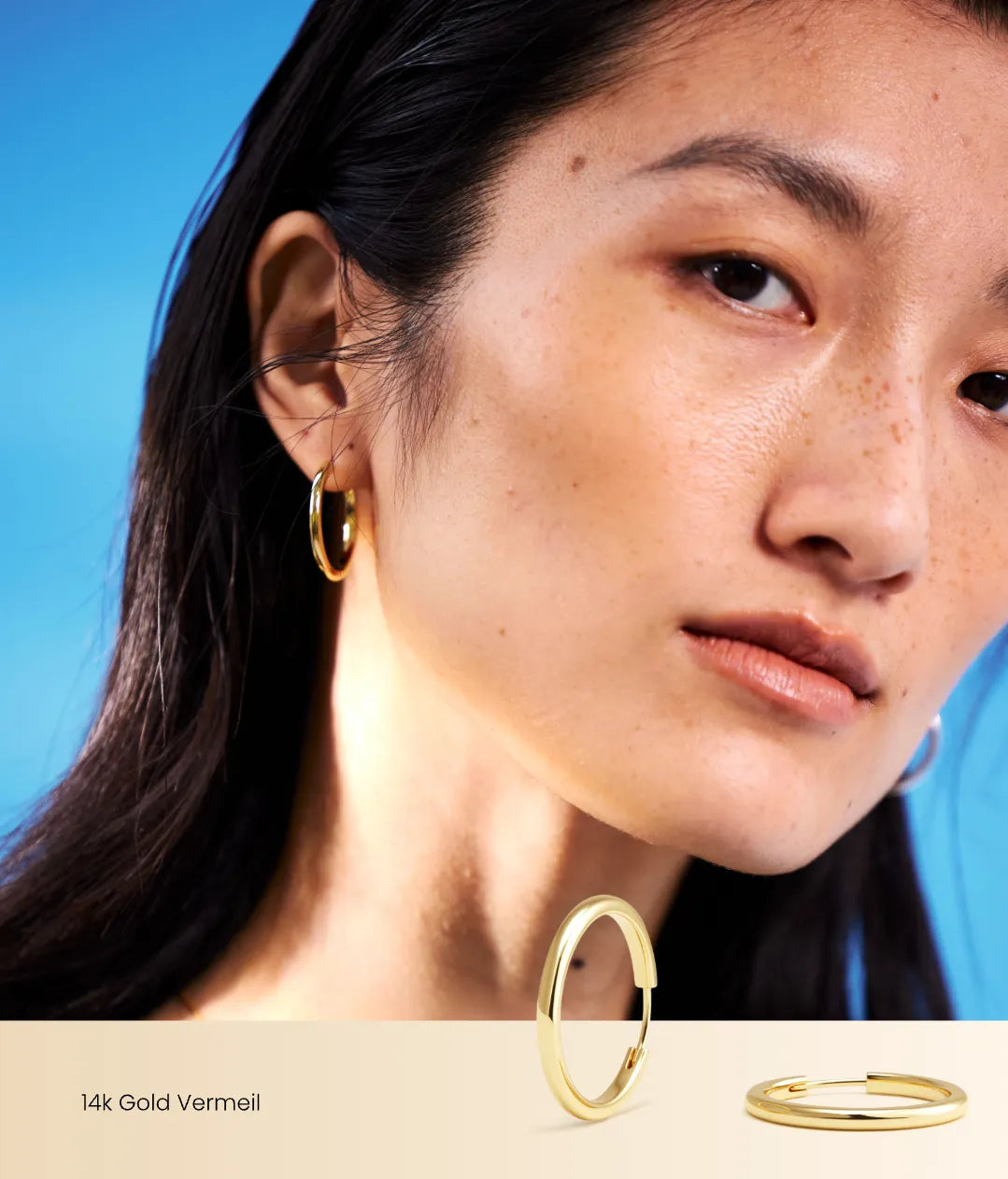 Close-up of a person wearing gold hoop earrings with a blue gradient background