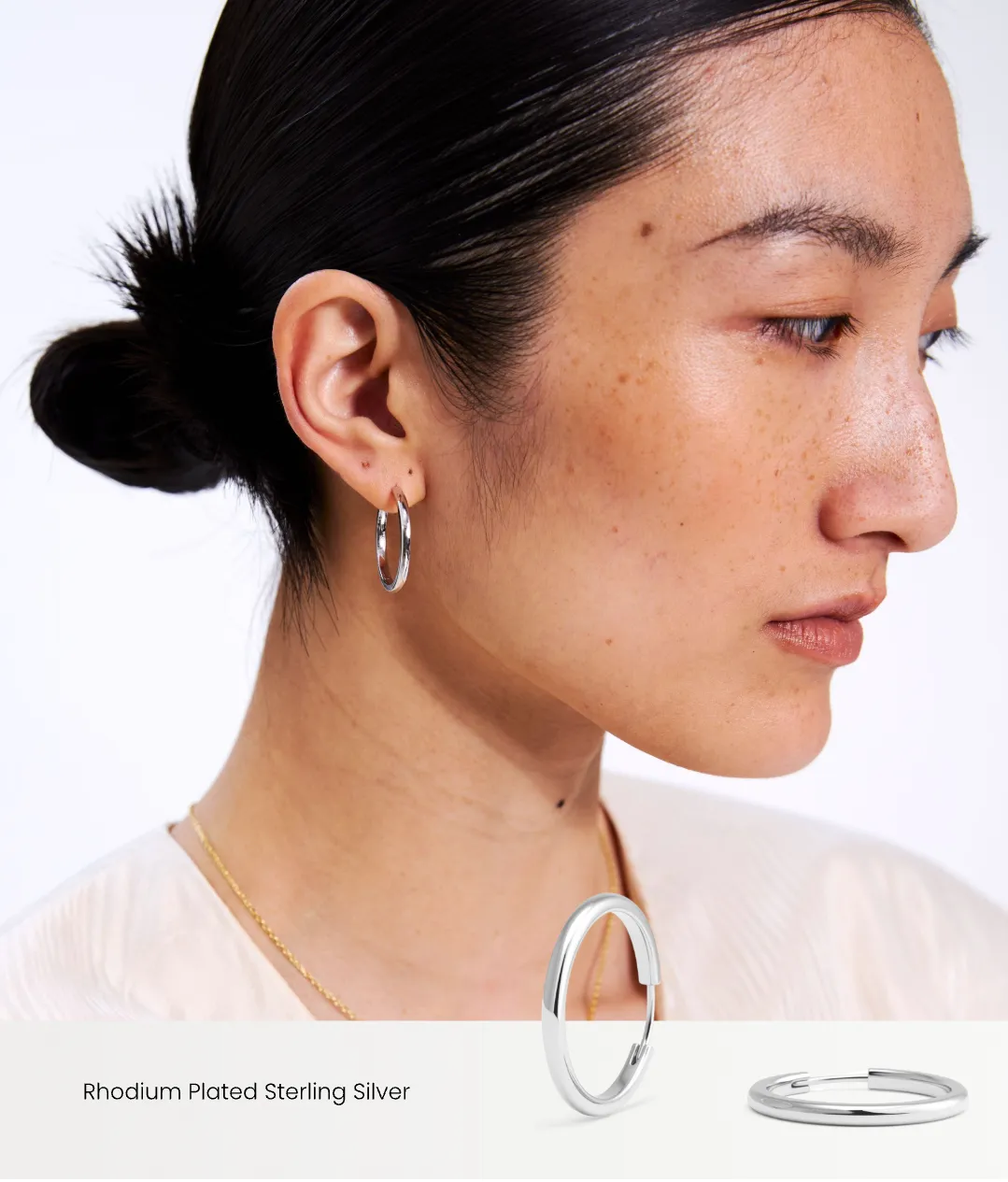 Close-up of a woman wearing silver hoop earrings with a plain background