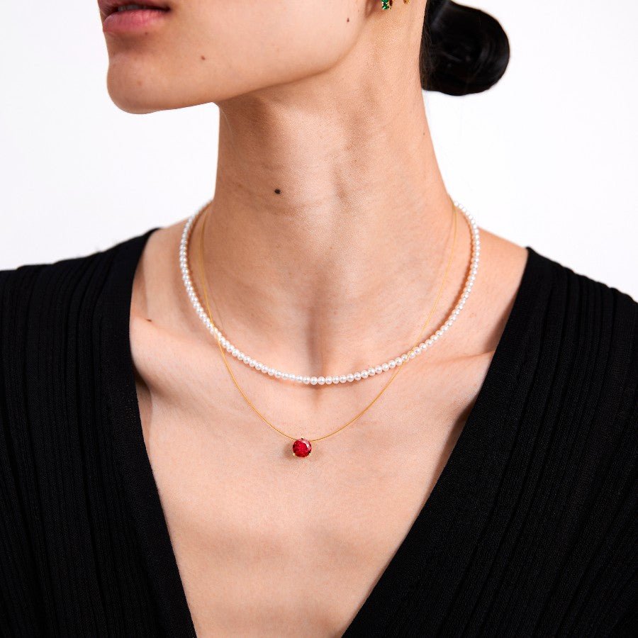 Woman wearing a pearl necklace and a wire necklace with ruby pendant