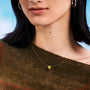Close-up of a person wearing a gold nylon necklace with a yellow sapphire against a blue background
