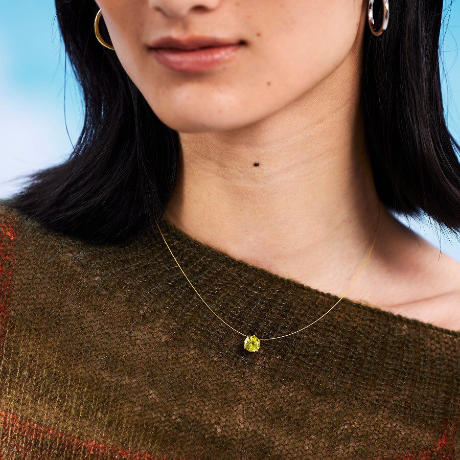 Close-up of a person wearing a gold nylon necklace with a yellow sapphire against a blue background