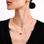 Close-up of a person wearing a pearl necklace and a blue sapphire necklace on a plain background