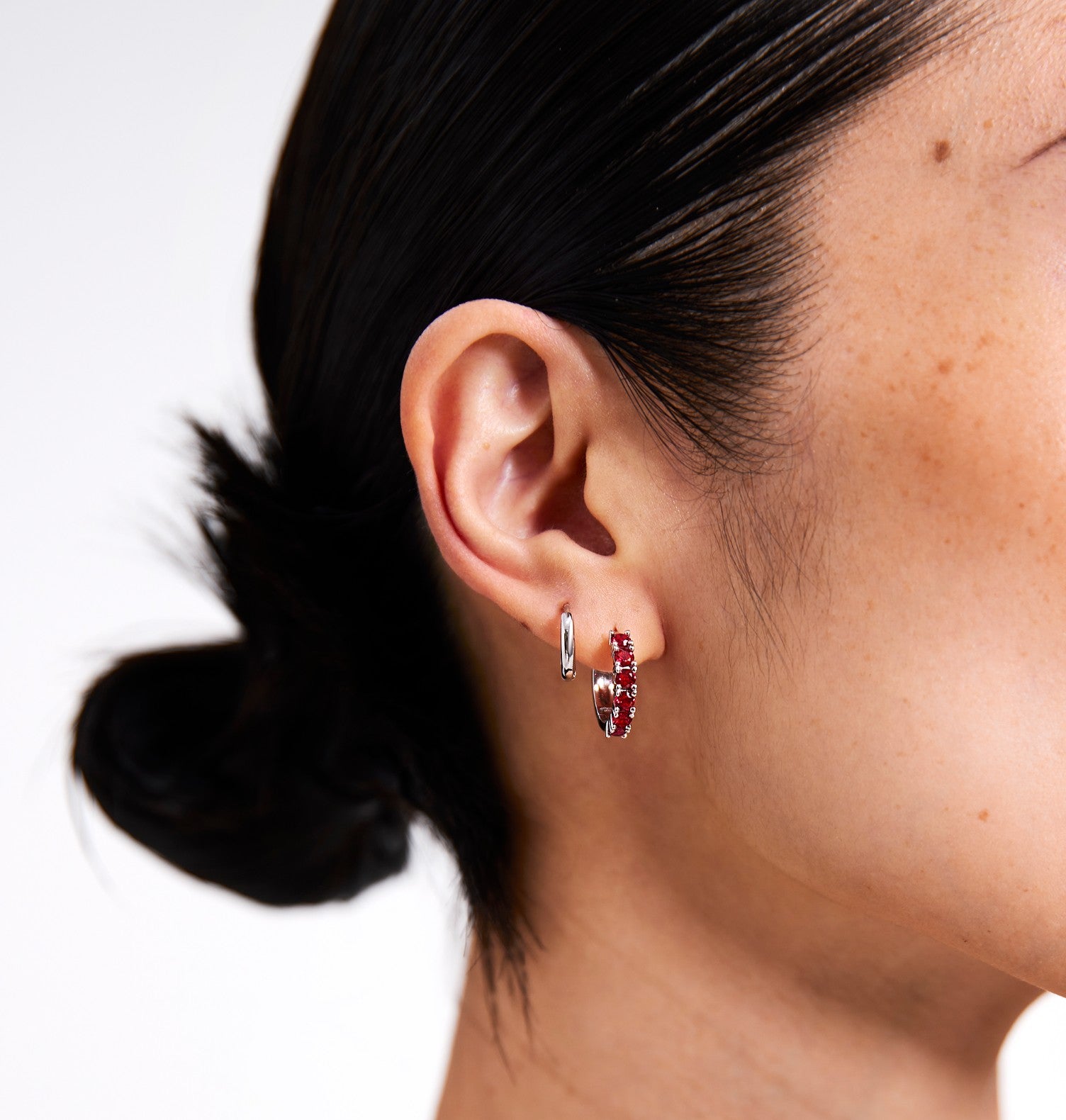 Close-up of a person wearing hoop earrings with a plain background