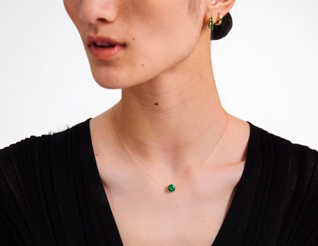 Person wearing a wire necklace with an emerald against a neutral background