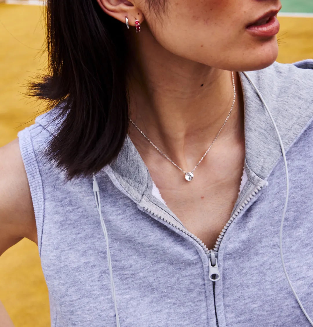 Person wearing a silver necklace with a white round sapphire against a yellow background