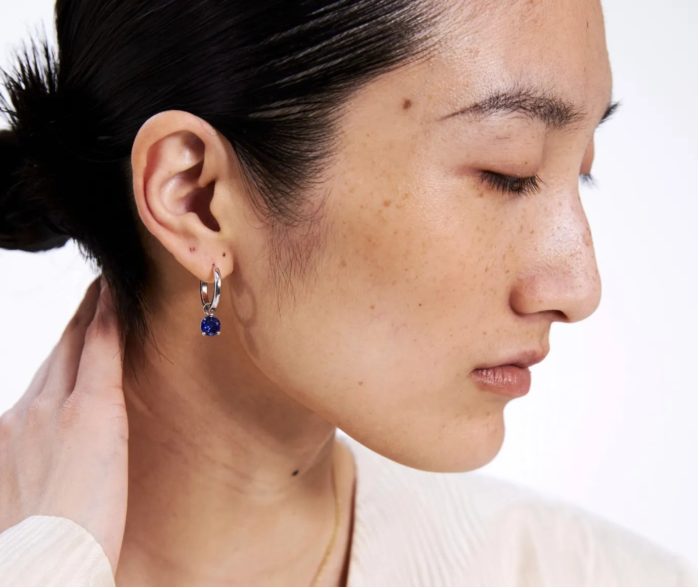 Close-up of a person wearing a silver earring with a blue gemstone on a white background