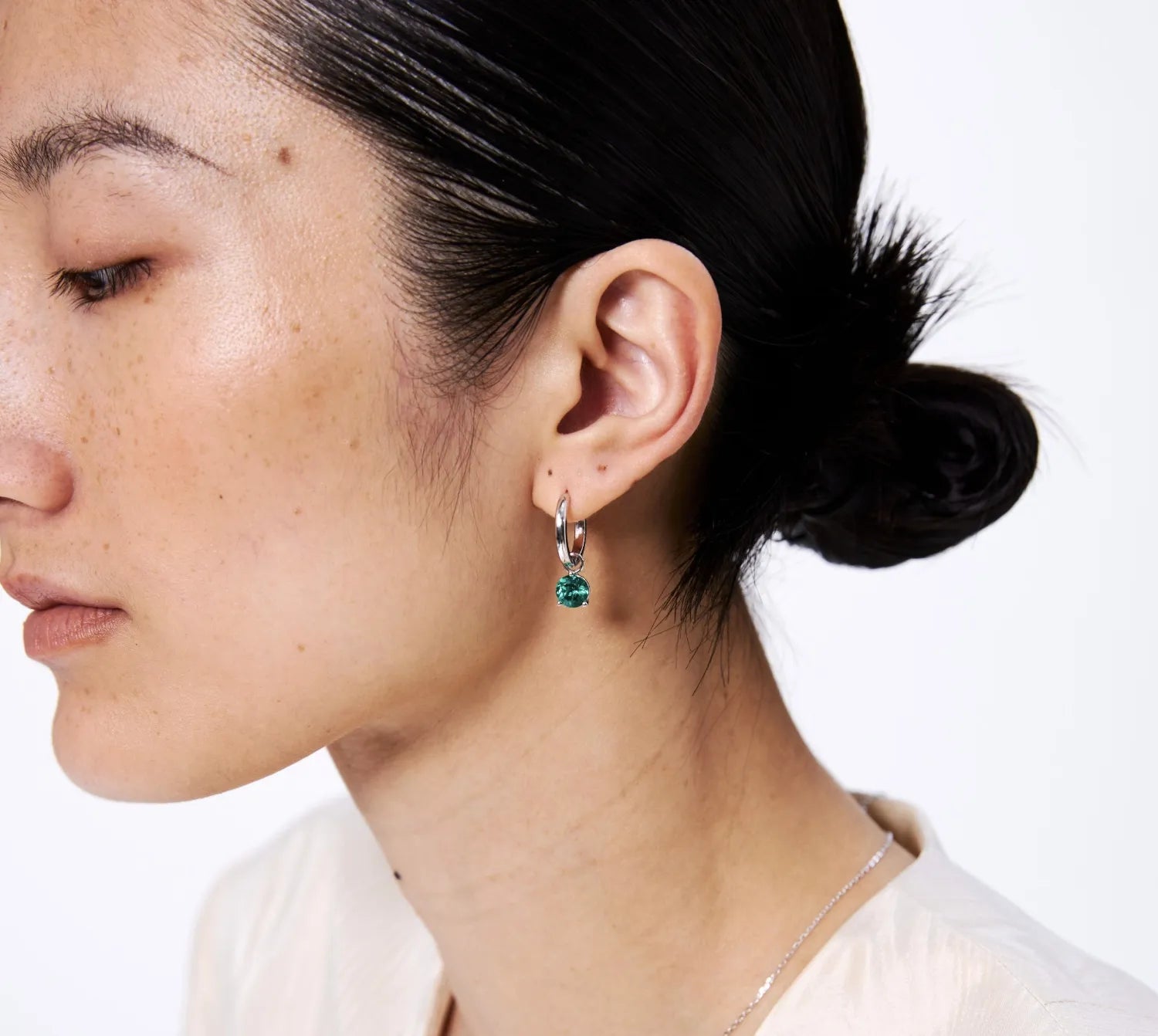 Close-up of a person wearing a silver earring with a green gemstone on a white background