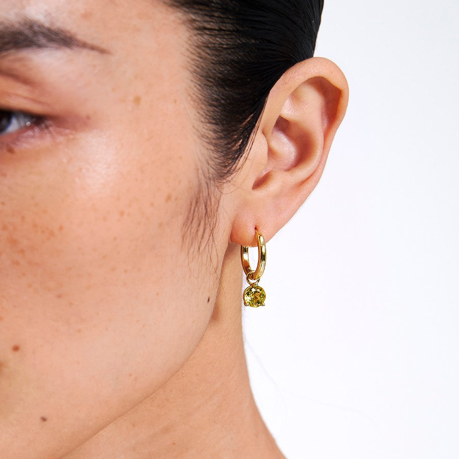 Close-up of a person wearing a gold earring with a yellow gemstone 