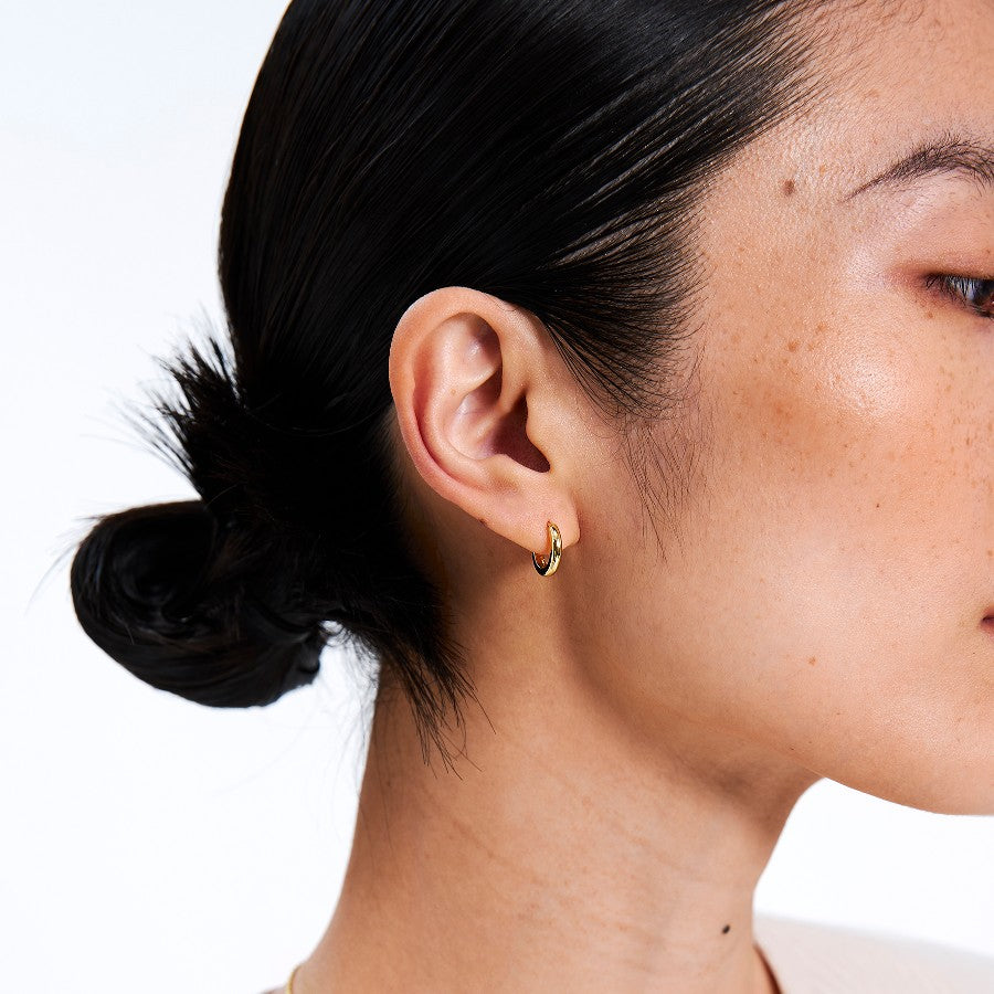 Close-up of a person wearing mini gold hoop earrings with a plain background