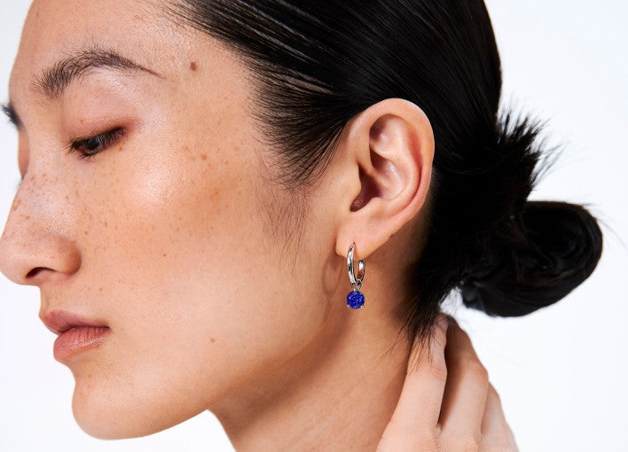 Close-up of a person wearing a silver earring with a blue gemstone on a white background