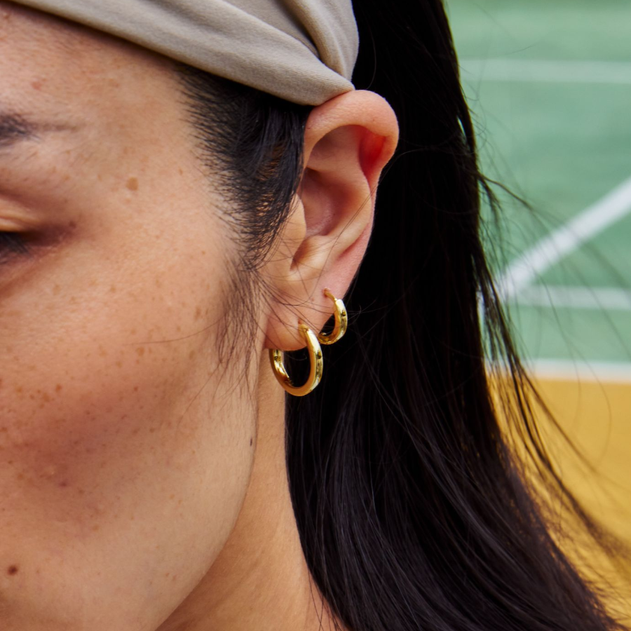 Close-up of a person wearing two gold hoop earrings with a blurred background