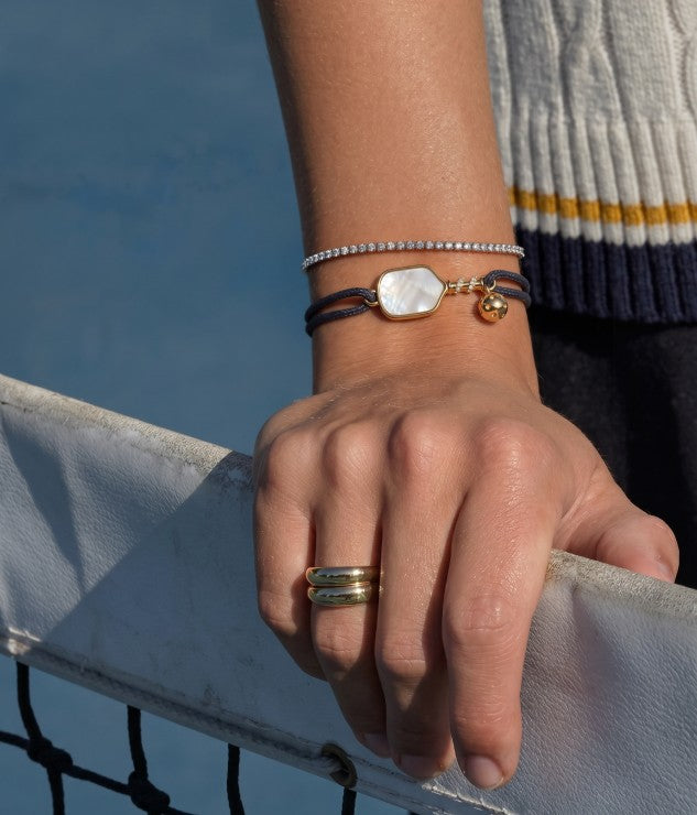 Hand wearing a Glint & Luck pickleball bracelet and ring with a blurred background
