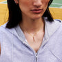 Person wearing a light gray zip-up hoodie with a gold bar necklace, standing on a basketball court.