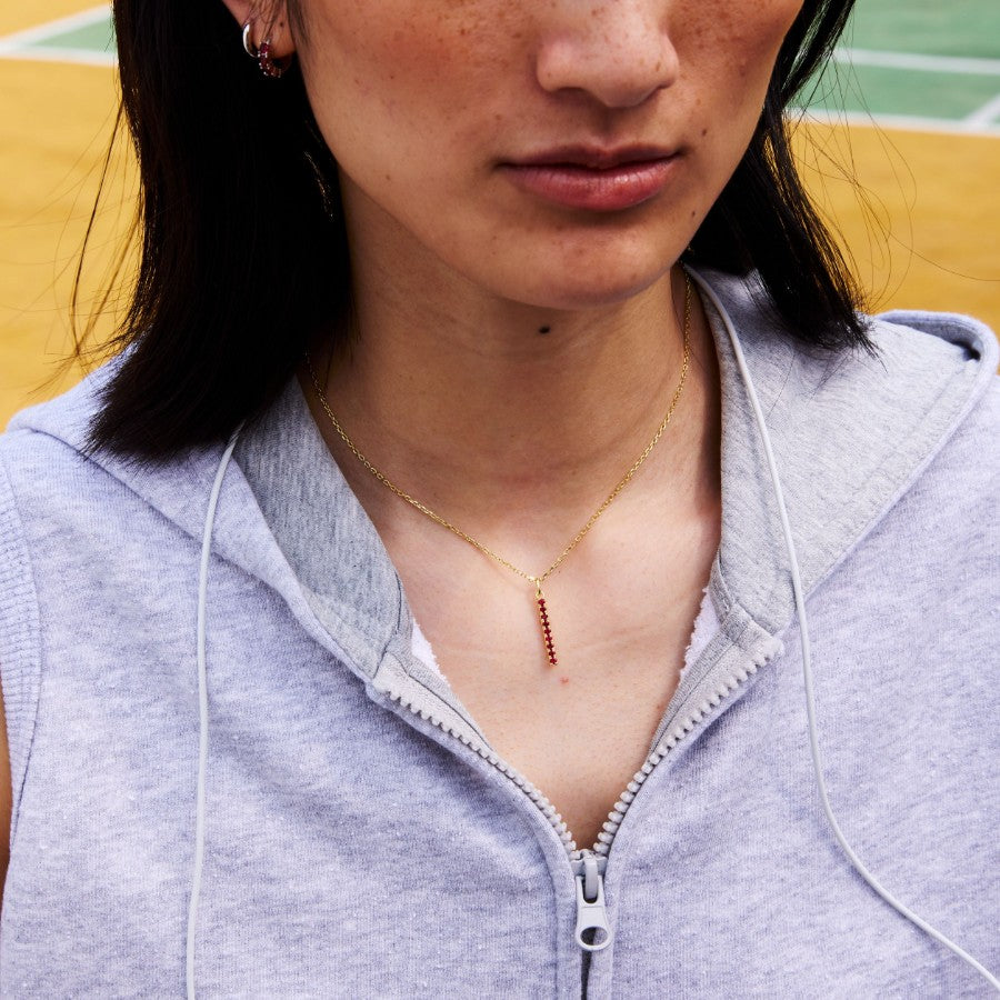 Person wearing a light gray zip-up hoodie with a gold bar necklace, standing on a basketball court.
