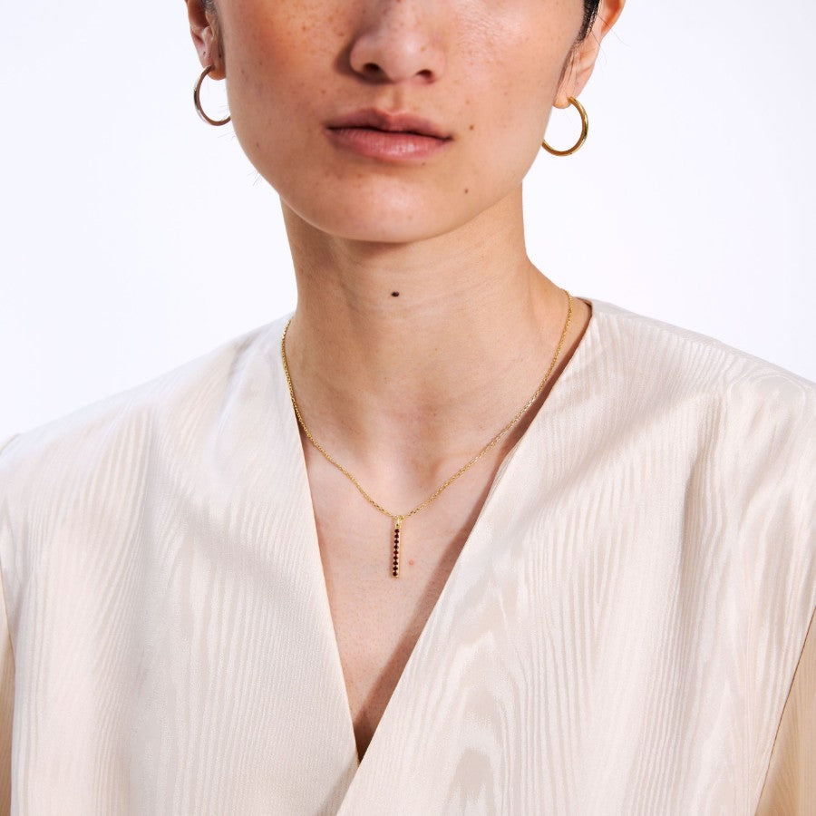 Close-up of a person wearing gold hoop earrings and a gold necklace with a pendant on a white background