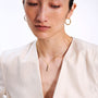 Person wearing gold hoop earrings and a delicate gold bar necklace on a white background
