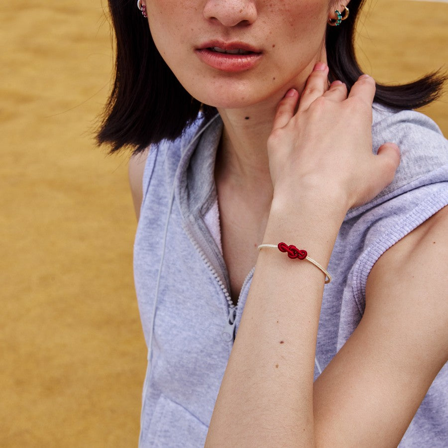 Woman wearing a white string bracelet with a red knot on a beige background