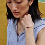 Woman wearing a white string bracelet with a red wukong knot on a yellow background