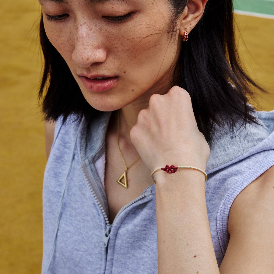 Woman wearing a white string bracelet with a red wukong knot on a yellow background