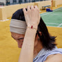 Person with a headband and another hand adjusting it on a sports court, wearing a white string bracelet with a red knot