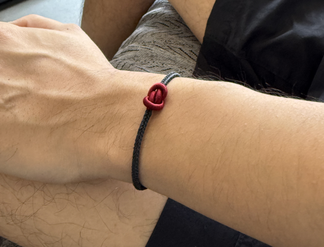 Close-up of a wrist wearing a black and red bracelet on a neutral background
