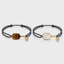 Two black cord bracelets with gemstone pickleball paddle charms on a light gray background