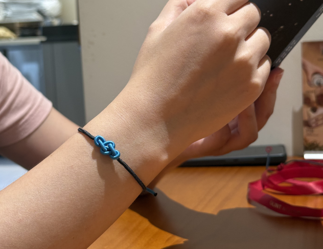Hand wearing a blue and black bracelet on a wooden surface with a blurred background