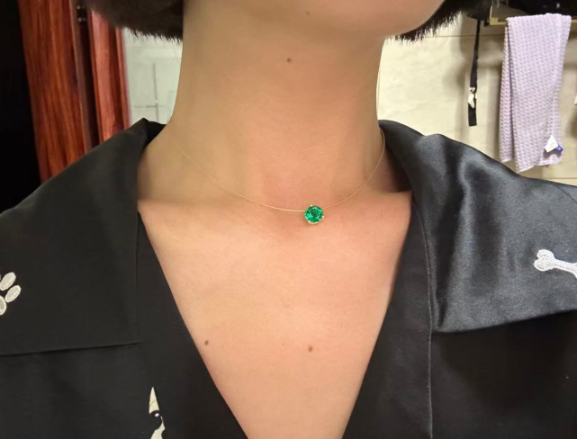 Person wearing a wire necklace with a green gemstone against a blurred indoor background