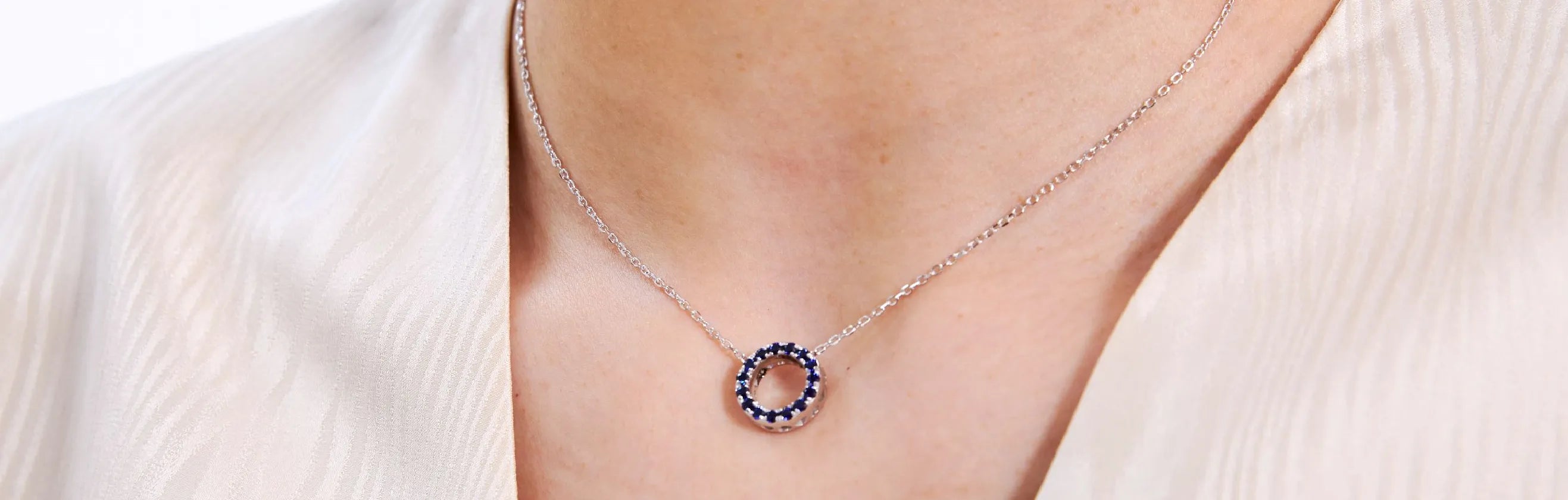 Silver necklace with a blue pendant on a person wearing a white blouse.