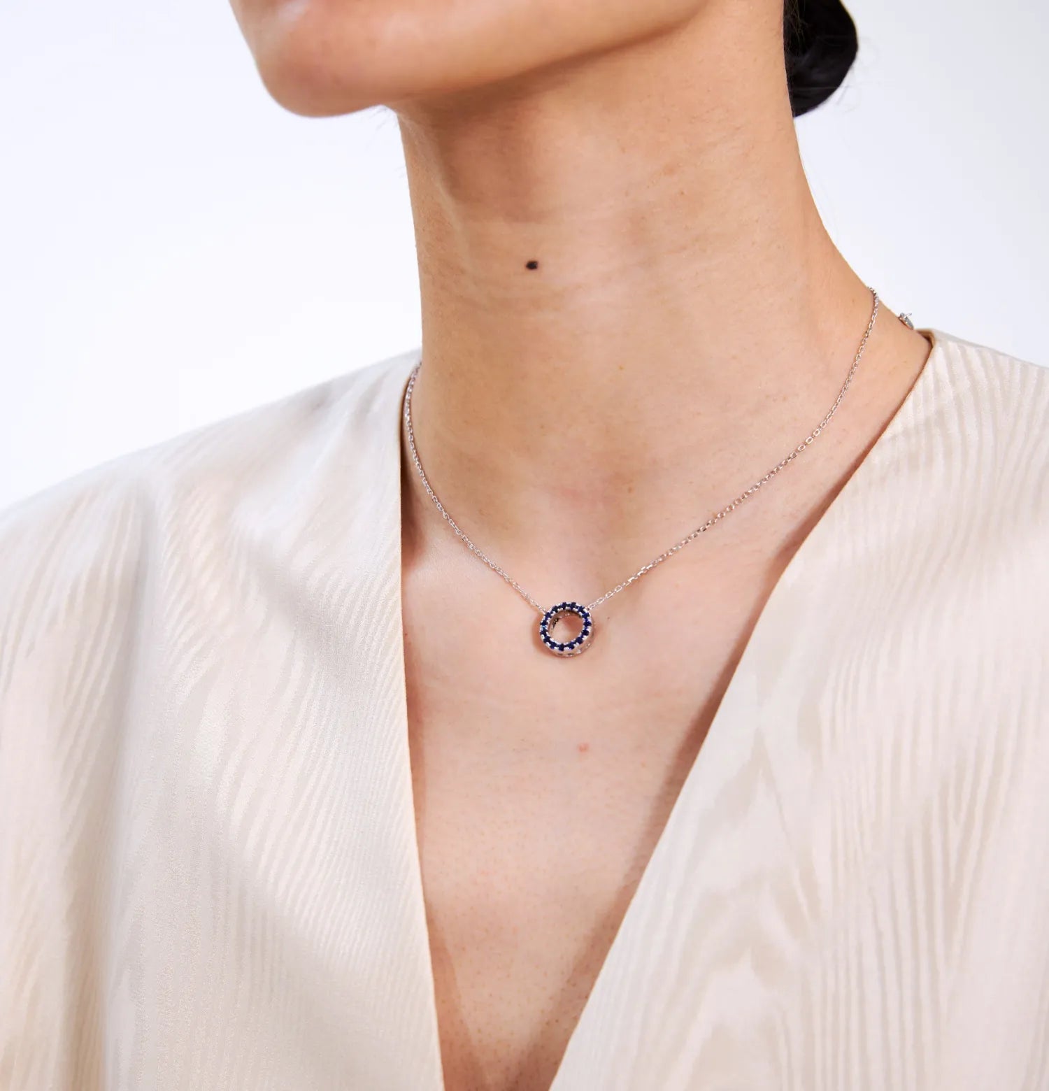 Silver necklace with a circular pendant worn by a person against a white background