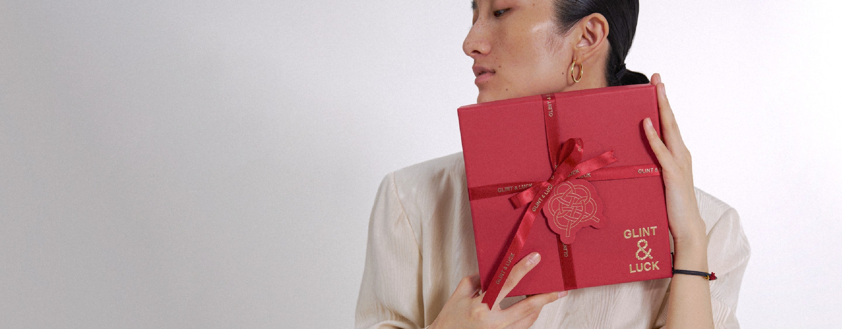 Person holding a red gift box with ' Glint & Luck' branding against a plain background