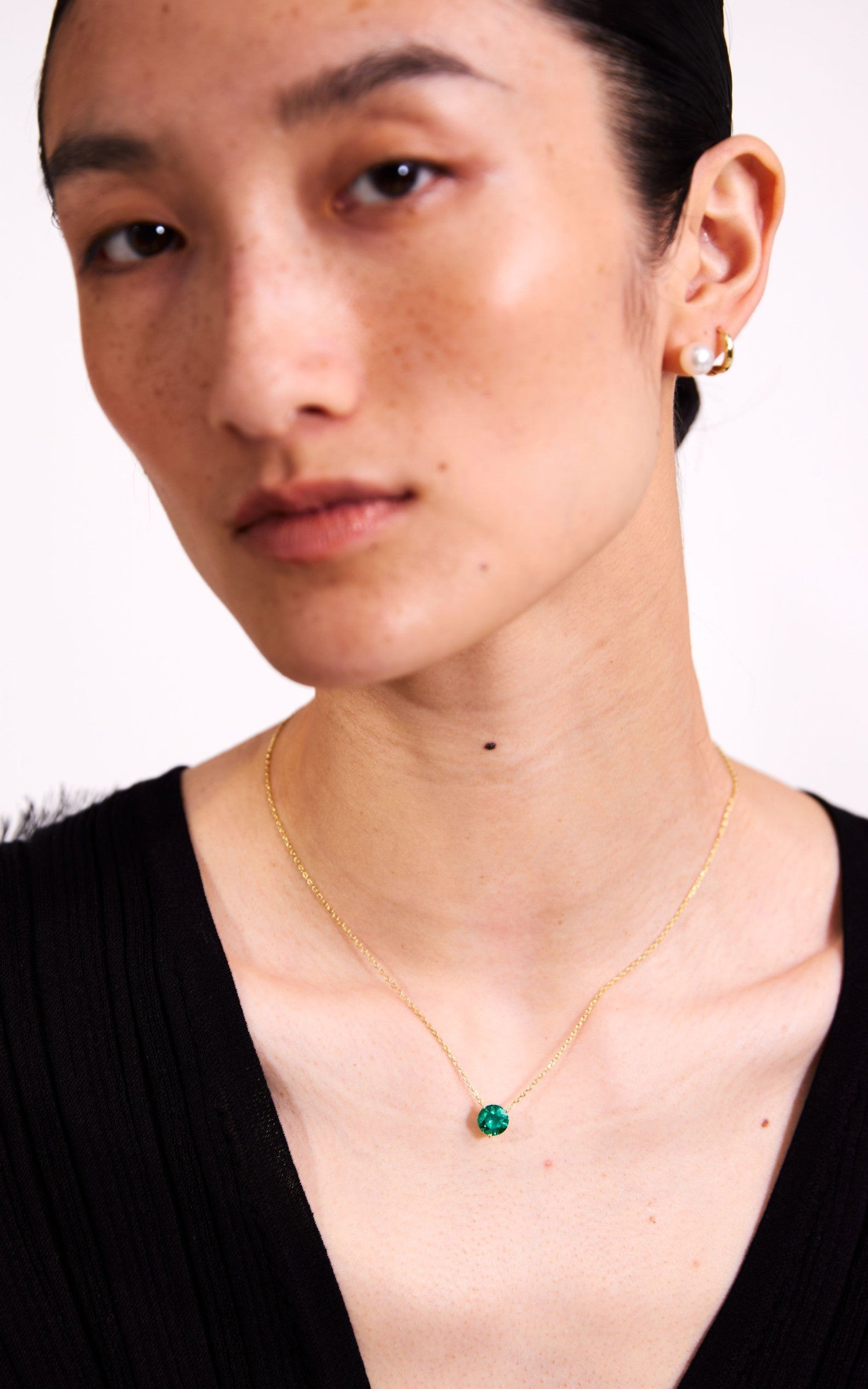 Close-up of a person wearing a gold necklace with a green pendant on a white background